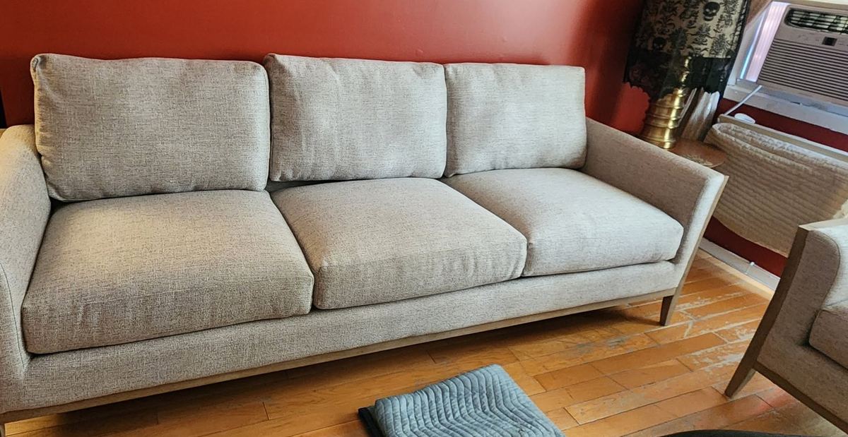 A modern three-seat sofa with a wood base, rebuilt and placed