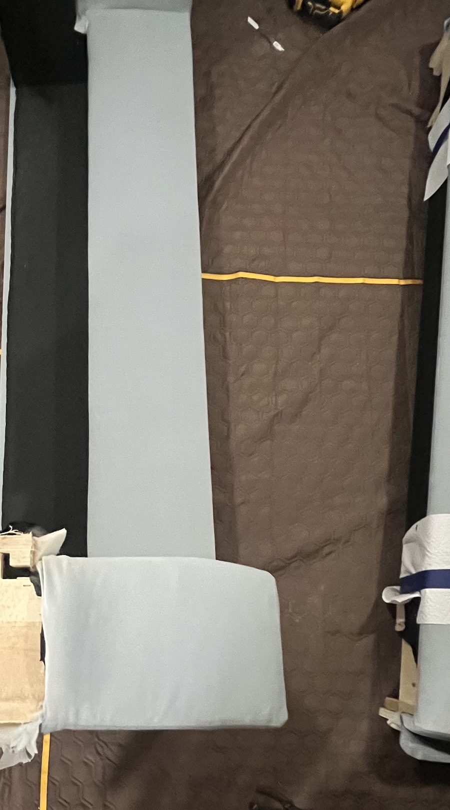 A sofa's back, arms and seat taken apart and laid out indoors on blankets, a drill beside them