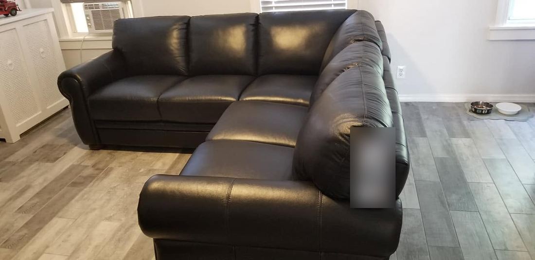 Black leather L-shaped sectional with rolled arms and loose back cushions on a gray wood-look floor