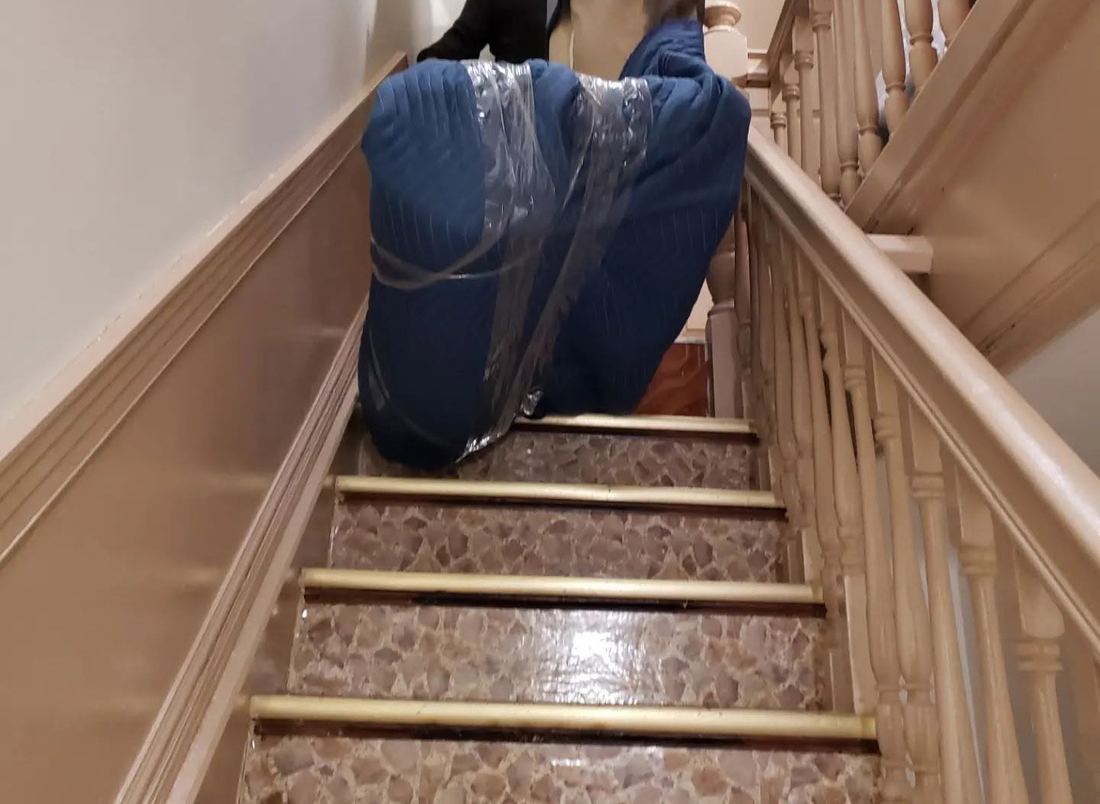Sofa wrapped in blue blankets and clear plastic on a narrow staircase with brass stair edges