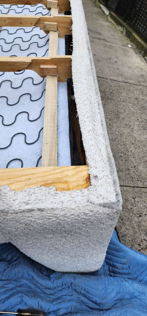 Close-up of an upholstered boucle sofa frame with exposed sinuous springs and wood rails on a blue pad