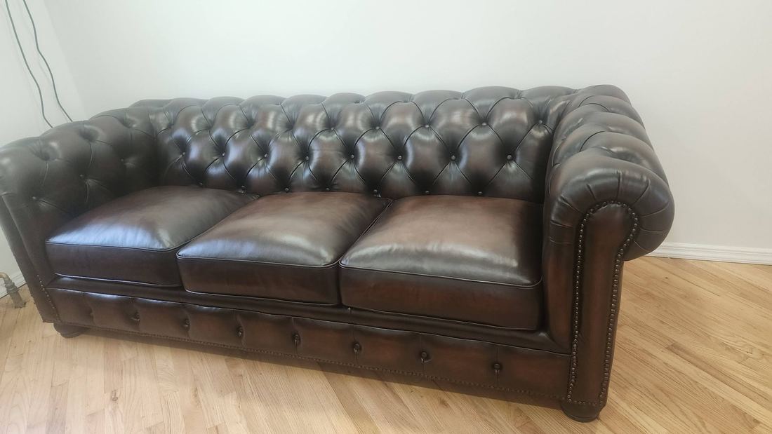 Brown tufted leather Chesterfield sofa with rolled arms and nailhead trim on a hardwood floor