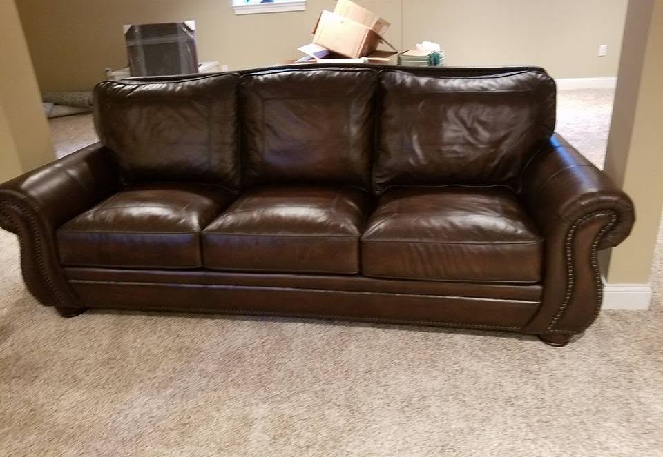 Brown leather three-seat sofa with rolled nailhead-trimmed arms on beige carpet