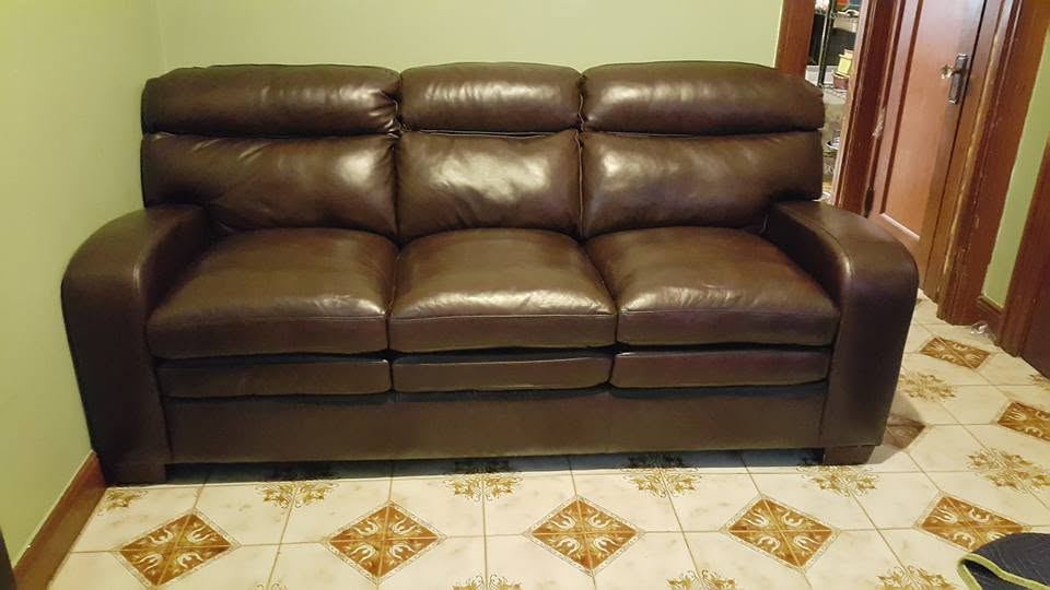 Brown leather three-seat sofa with square padded arms against a pale green wall on a patterned tile floor