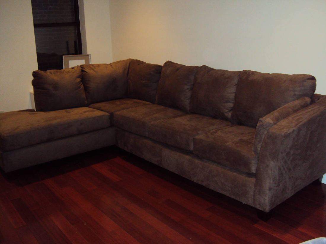 Brown microsuede L-shaped sectional with a chaise and loose back cushions on a red-toned hardwood floor