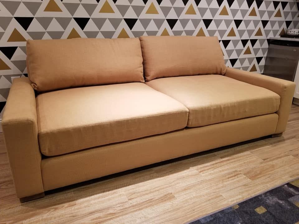 Camel fabric two-seat sofa with square arms and loose back cushions against black, grey and gold triangle wallpaper