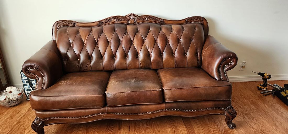 Brown tufted leather sofa with a carved wooden crest, rolled nailhead arms and carved cabriole legs
