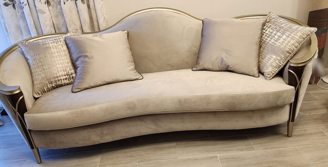 Curved champagne velvet sofa with a gold-toned wood frame, tapered metal legs and four silver pillows