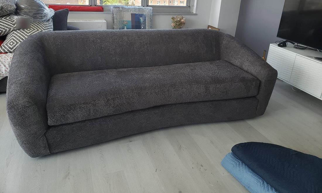 Curved charcoal boucle sofa with a single bench cushion on a light wood-look floor, padded blankets nearby