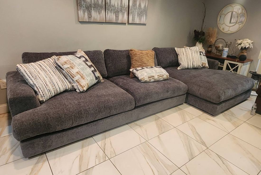 Charcoal gray sectional sofa with a right-side chaise and patterned pillows on white marble-look tile