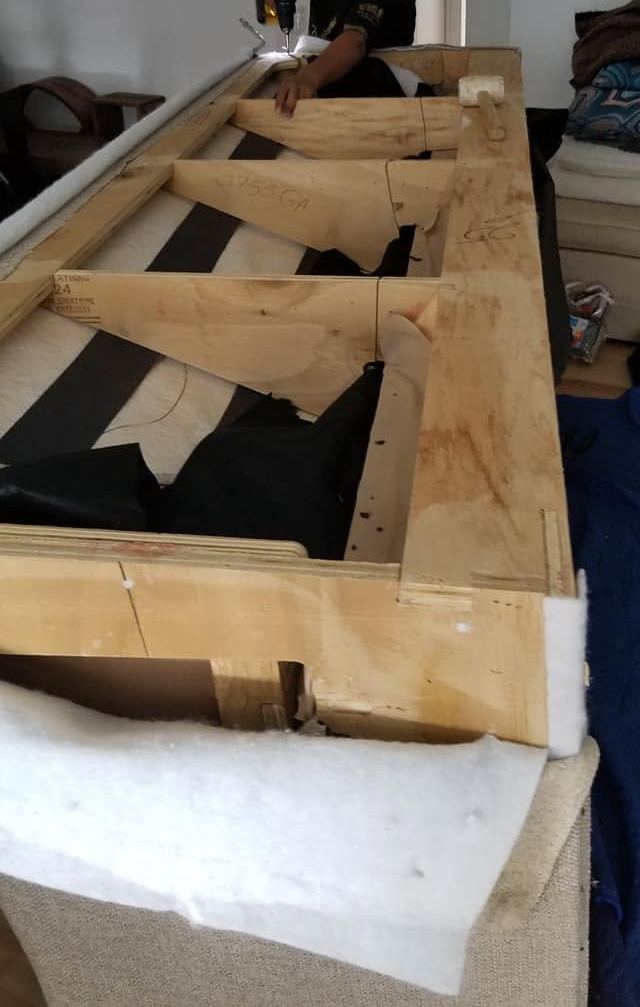 Arm and cordless drill working on an opened plywood sofa frame lined with webbing and batting