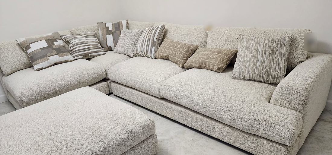 Cream boucle L-shaped sectional with a large matching ottoman and assorted neutral pillows