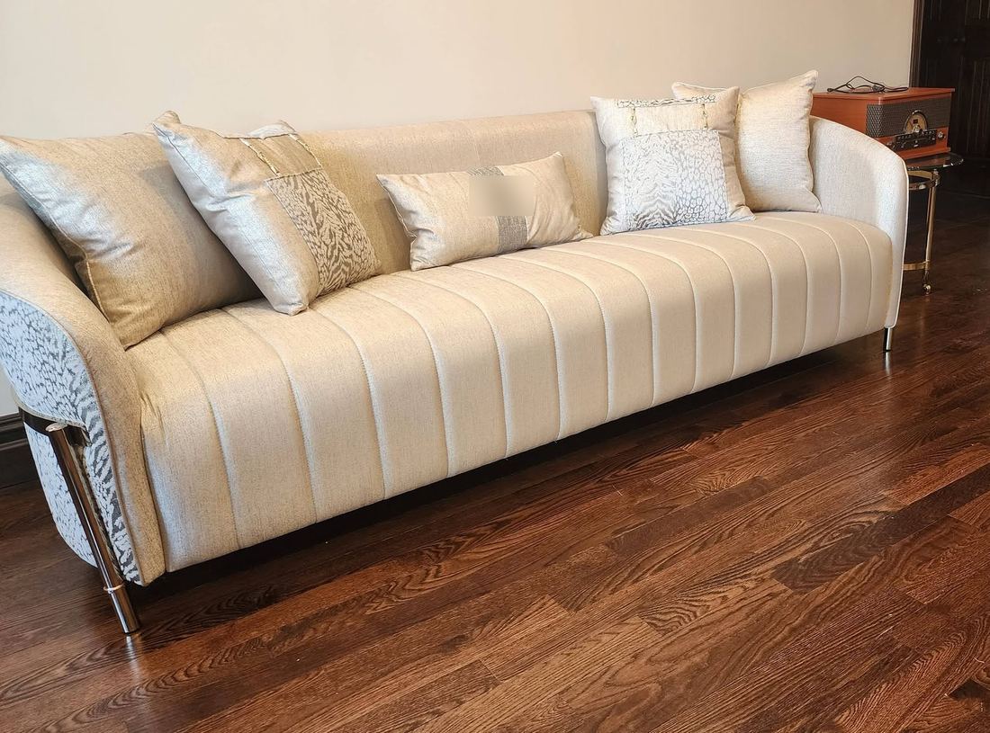 Cream channel-tufted sofa with chrome legs and silver-toned pillows on a dark hardwood floor
