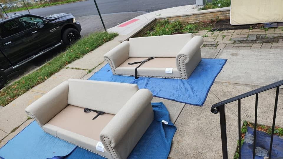 Two cream sofas with rolled nailhead arms and bare seats resting on blue blankets on a sidewalk