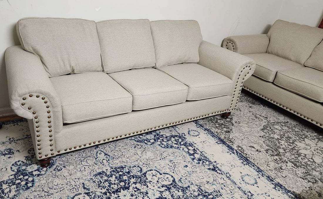 Cream rolled-arm sofa and matching loveseat with brass nailhead trim on a blue patterned rug