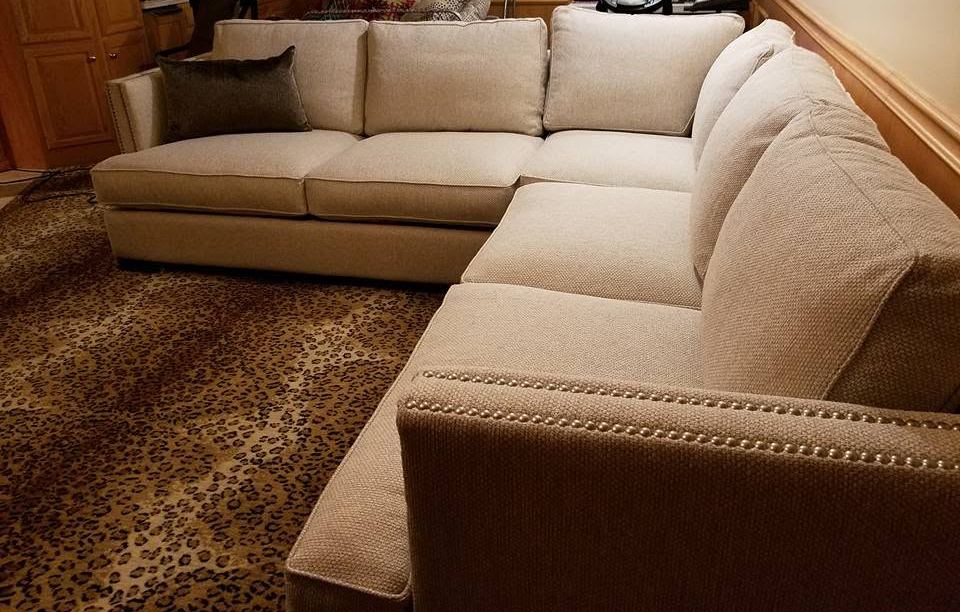 Cream fabric L-shaped sectional with nailhead trim along the arm, on a leopard-print carpet in a wood-paneled room