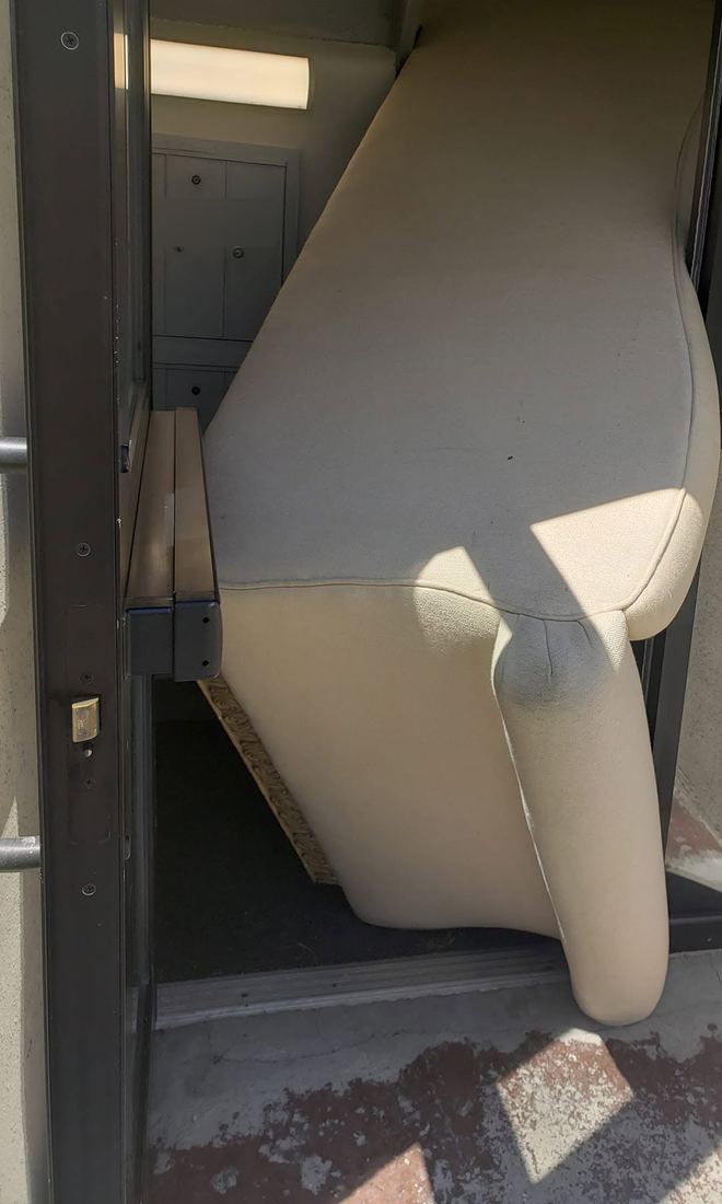Cream sofa tipped on its side and angled arm-first through a narrow glass-and-metal entry doorway