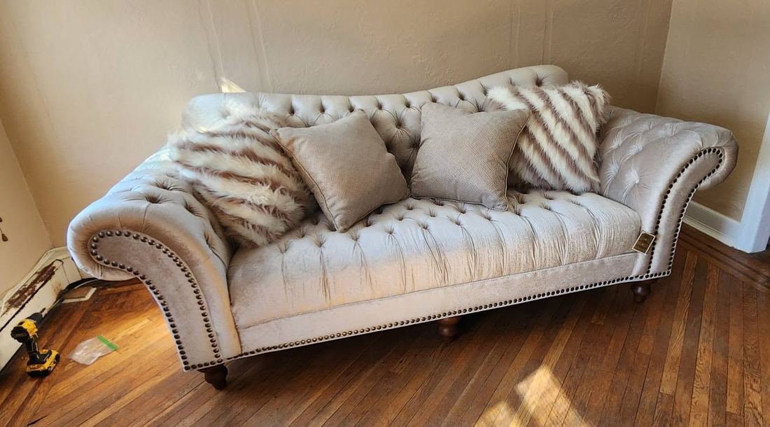 Cream tufted camelback sofa with rolled nailhead arms and fur pillows on a sunlit hardwood floor