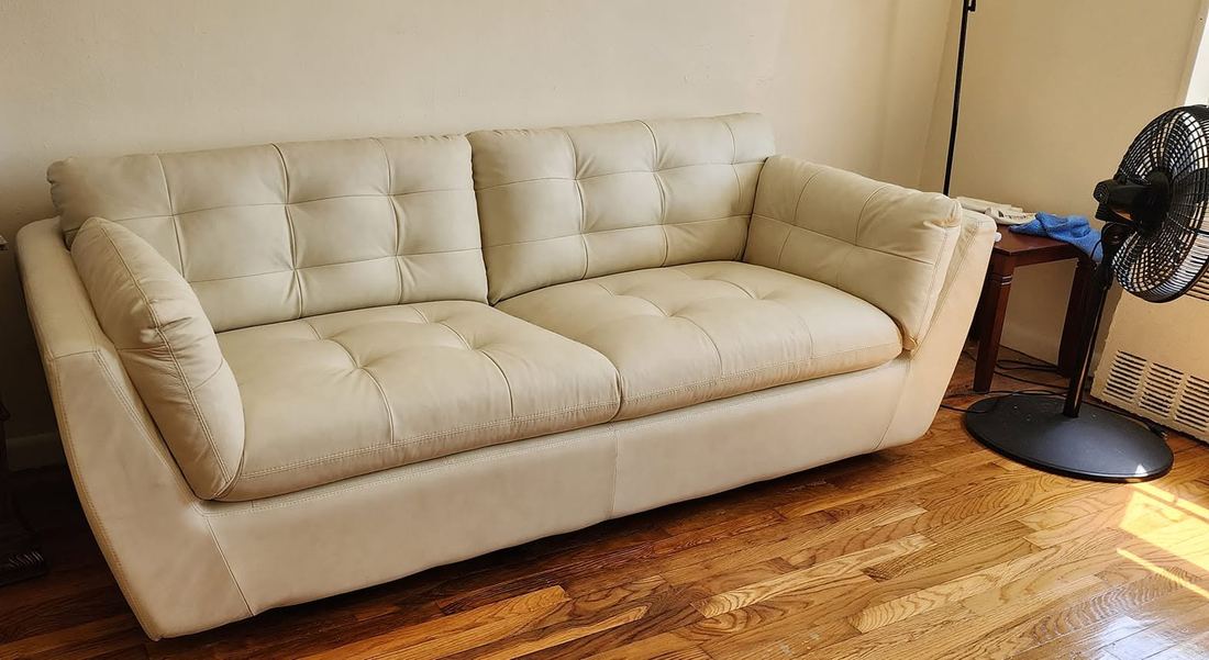Cream tufted leather sofa with angled arms and loose back cushions on a sunlit hardwood floor