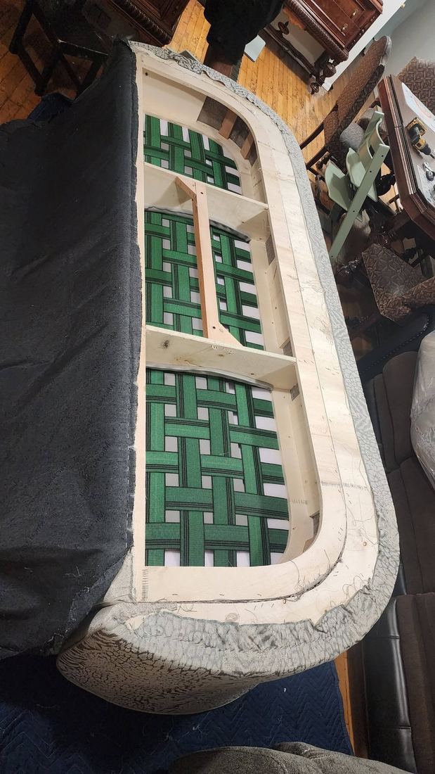 Overhead view of a curved sofa with its upholstery opened, exposing the plywood frame and green woven webbing