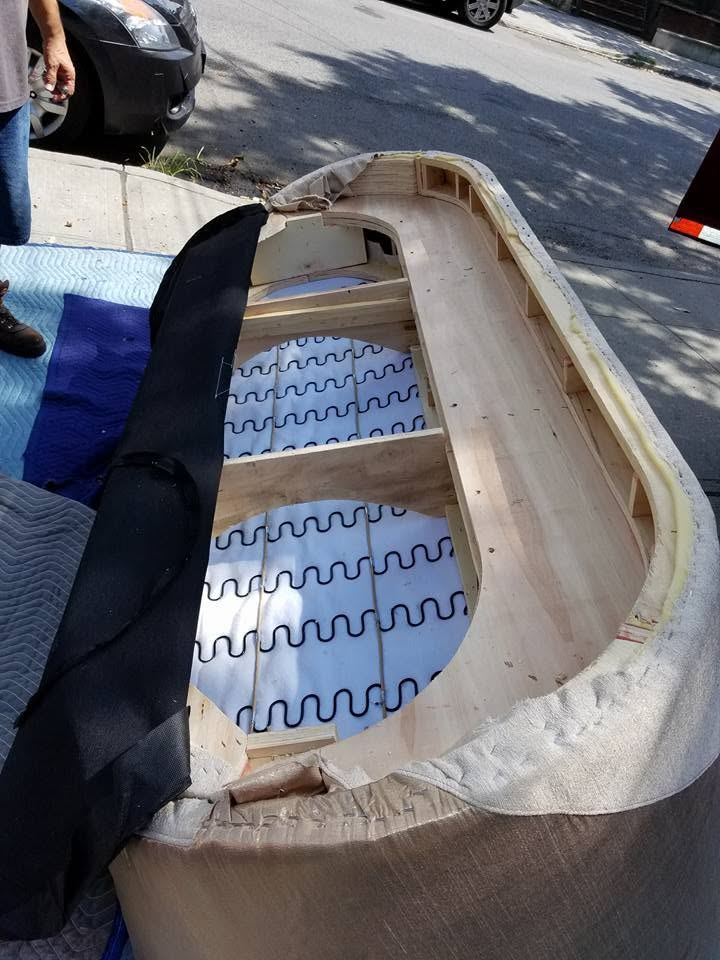 Curved sofa section on padded blankets on a sunny sidewalk, dust cover pulled back to show wood frame and zigzag springs