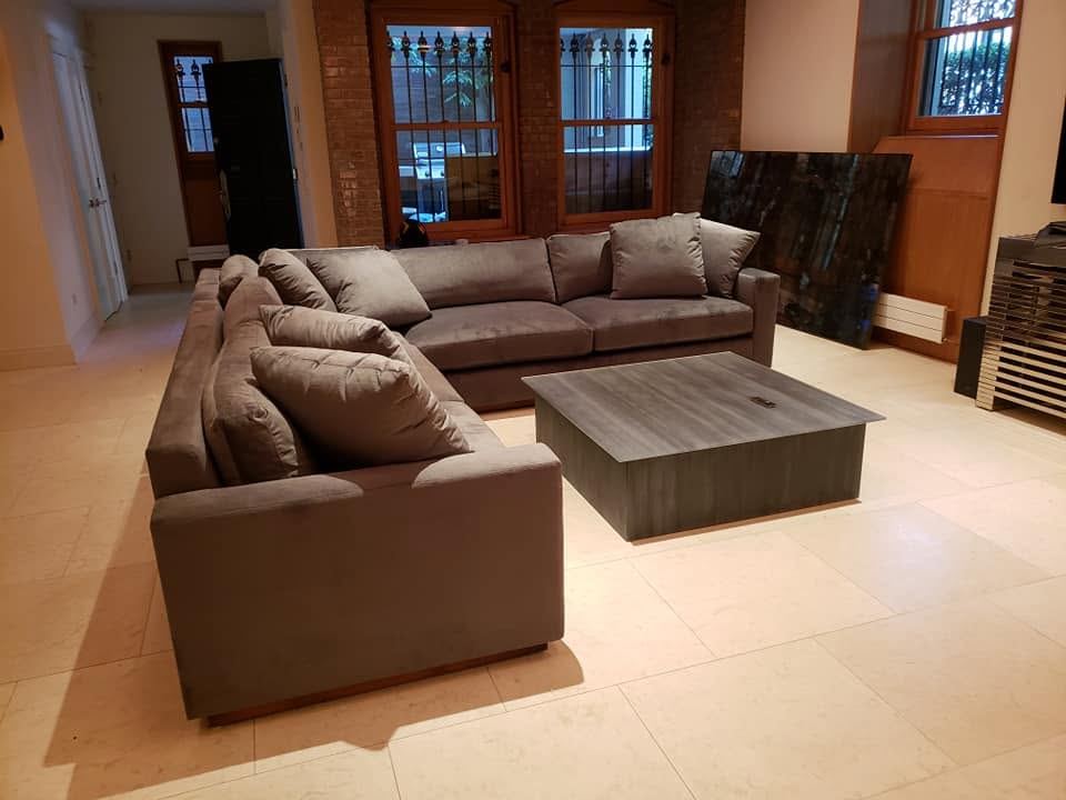 Gray L-shaped sectional with plush pillows around a square gray coffee table on a pale tile floor