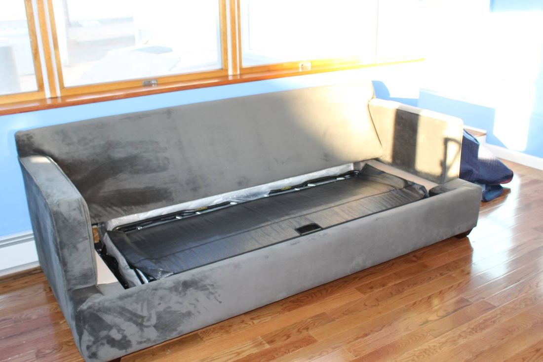 Gray microsuede sleeper sofa with seat cushions off, showing the folded bed mechanism, on a hardwood floor