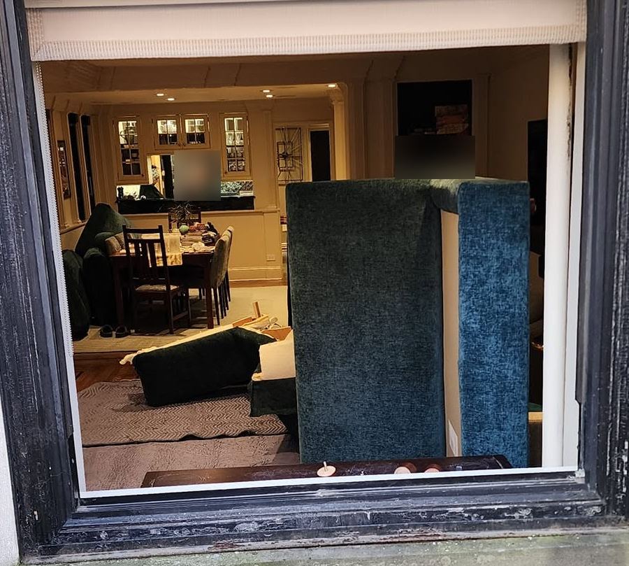 View through an open window of a green chenille sofa section standing upright, other pieces on padded blankets