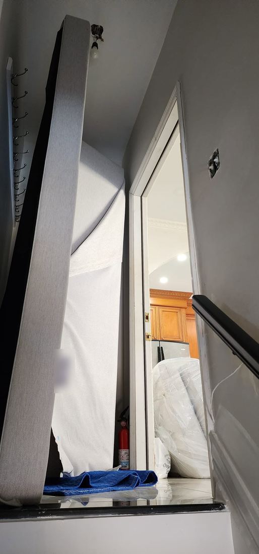 Two grey sofa pieces stood on end at the top of a stairwell beside a narrow doorway