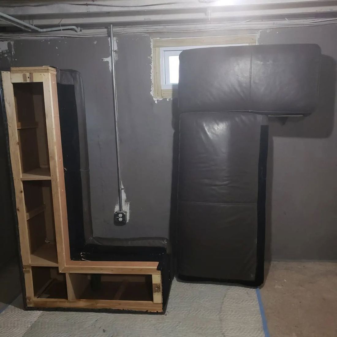 Bare wood L-shaped sectional frame in a basement, next to two dark leather upholstered pieces propped against the wall