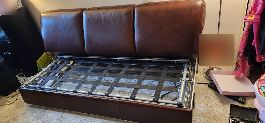 Brown leather sleeper sofa with its metal fold-out bed frame extended and a socket set on the carpet beside it