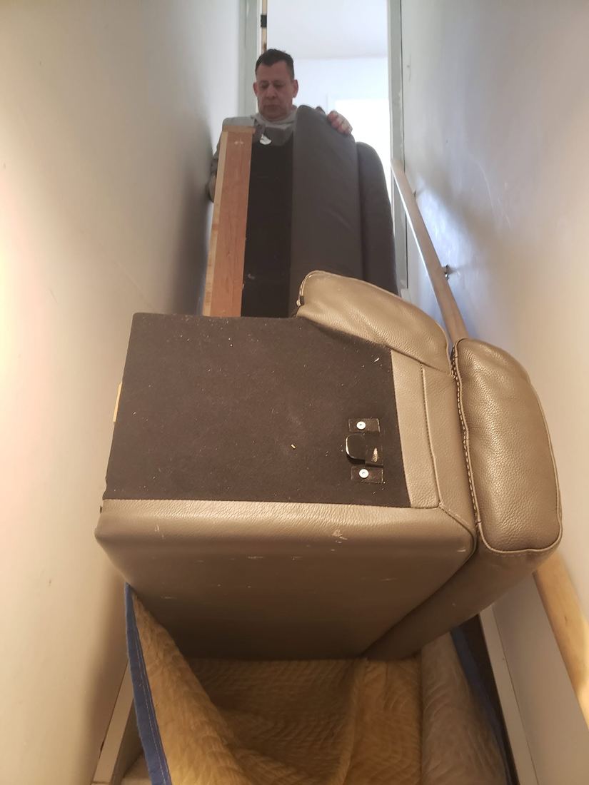Gray leather sofa sections stand on end in a narrow staircase as a crew member steadies the back piece
