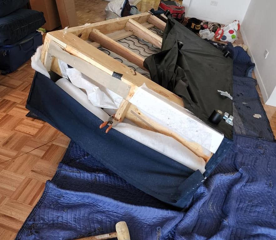 Navy sofa lying on blue blankets with fabric pulled back to show its wood frame, springs and a clamp