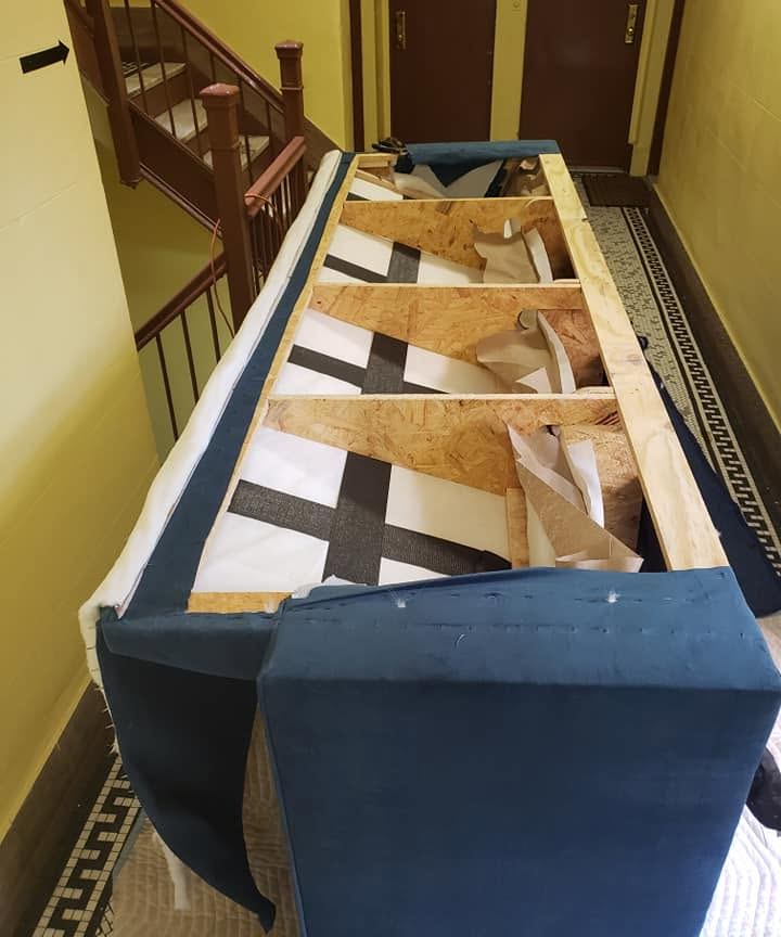 Navy sofa in a tiled building hallway with fabric removed to show the wood frame and crisscross webbing