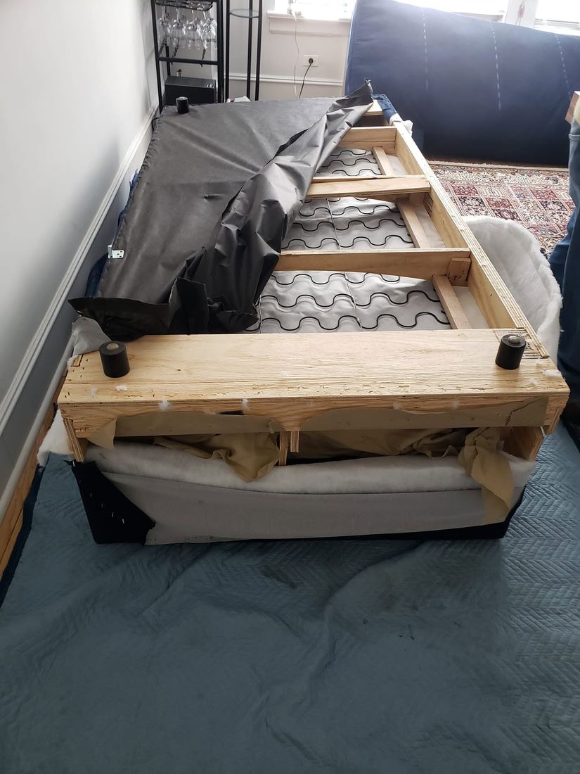 Navy sofa turned upside down on blue blankets, black dust cover pulled back to reveal wood rails and zig-zag springs