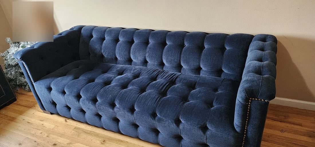 Navy blue tufted velvet Chesterfield sofa with brass nailhead trim on a light hardwood floor