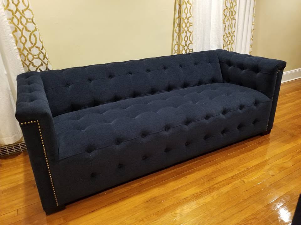 Navy button-tufted tuxedo sofa with straight high arms and brass nailhead trim in front of white and gold curtains