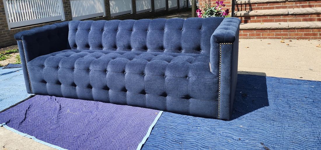 Navy tufted tuxedo sofa with nailhead trim resting on padded blankets on a sunny sidewalk