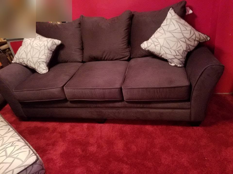 Plum fabric three-seat sofa with two white-and-gray patterned pillows, against a red wall on red carpet