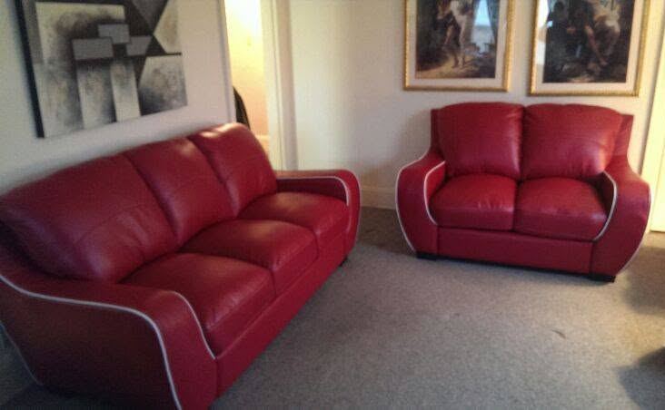 Red leather three-seat sofa and matching loveseat with white piping, arranged in a living room on gray carpet