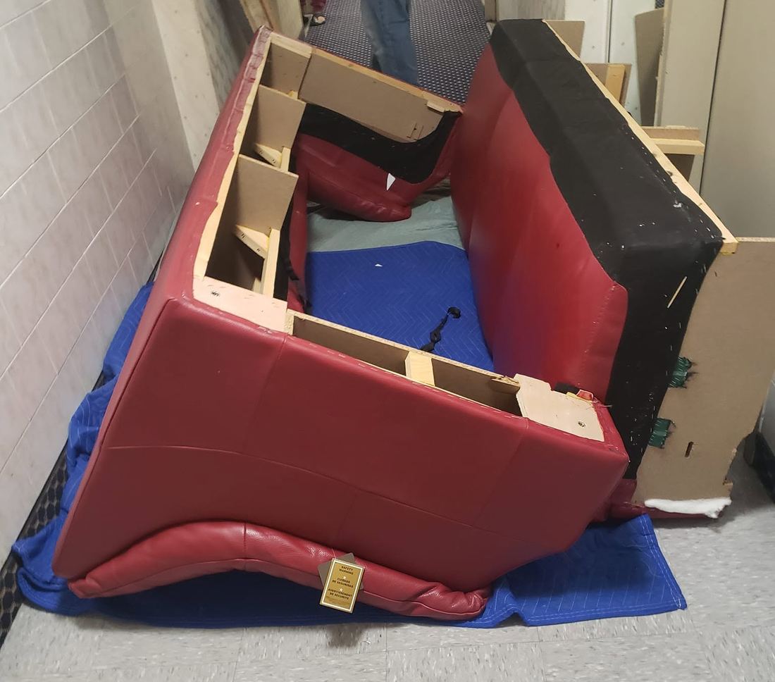 Red leather sofa in pieces on padded blankets in a narrow hallway, its inner wood frame exposed