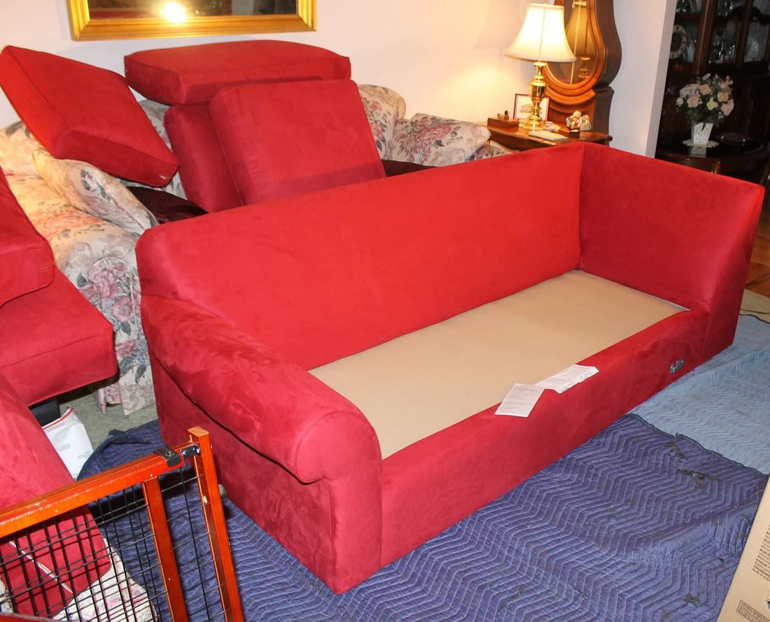 Red microfiber sofa with seat and back cushions removed, resting on blue padded blankets in a furnished living room