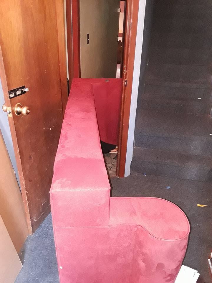 Red L-shaped sectional piece standing on end as it goes through a narrow doorway beside a staircase