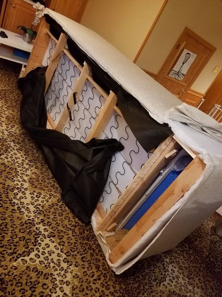 Cream sectional piece tipped on its side, black dust cover pulled back to show wooden frame, zigzag springs and blue foam