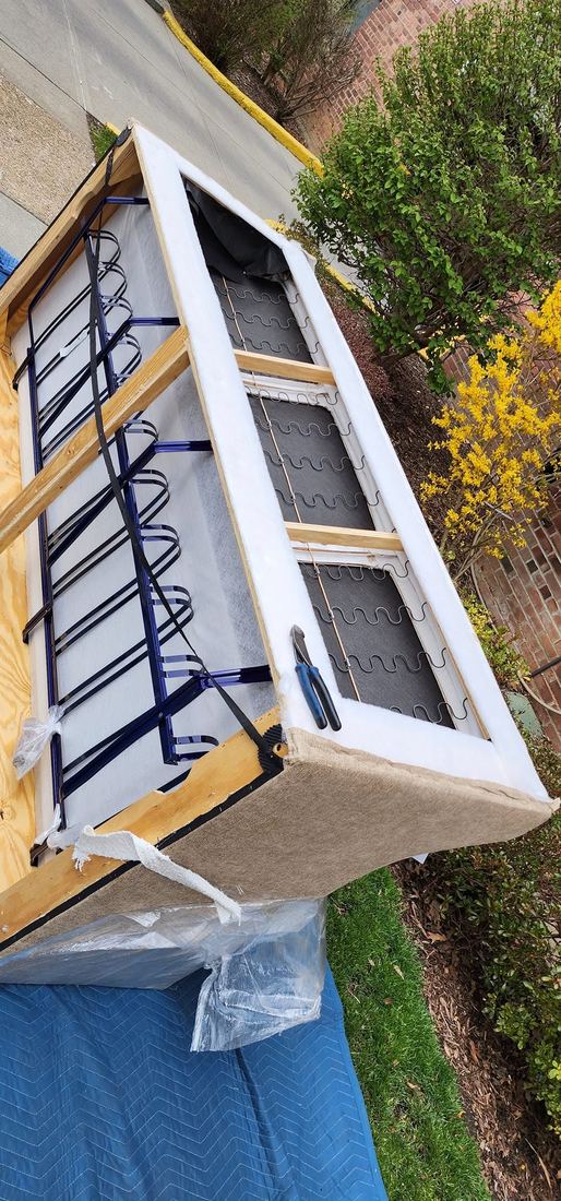Sleeper sofa opened on padded blankets outdoors, exposing the blue metal bed mechanism and zigzag springs