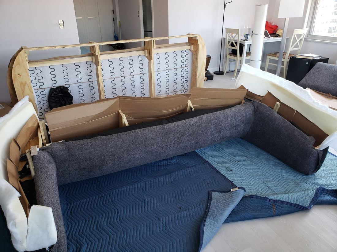 Sofa in pieces on padded blankets: wood back frame with zigzag springs behind the opened grey base and arms