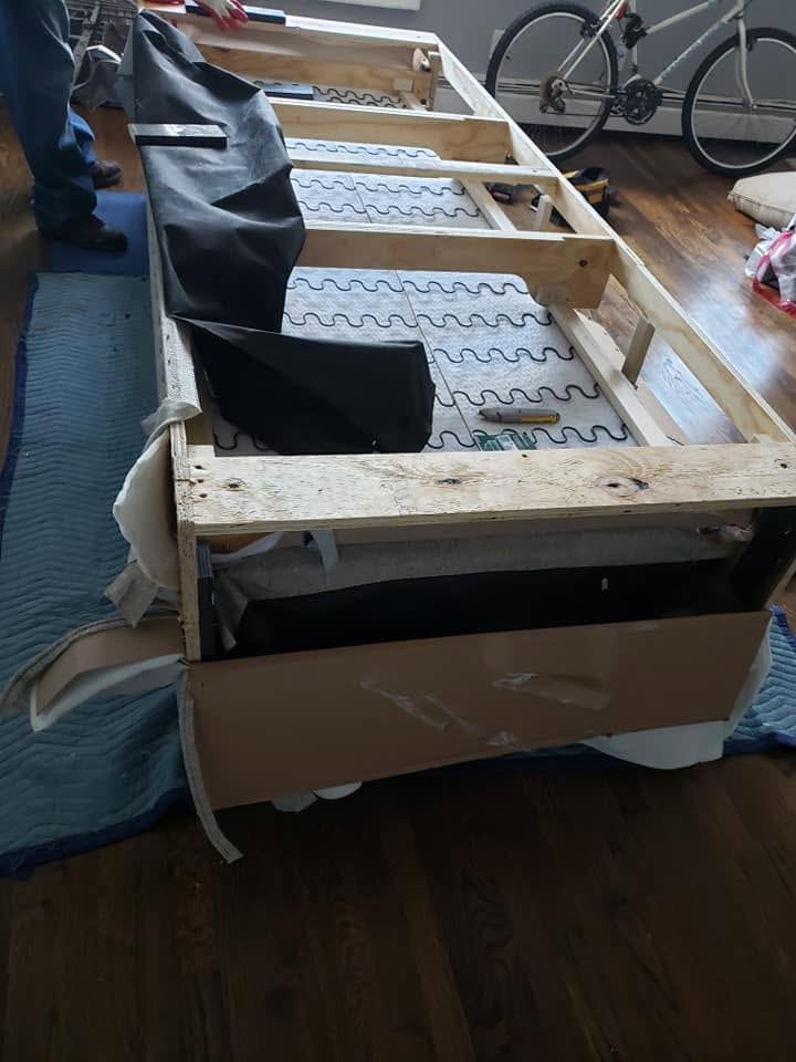 Opened sofa frame showing wood rails, zigzag springs and pulled-back dust cover, resting on protective blankets