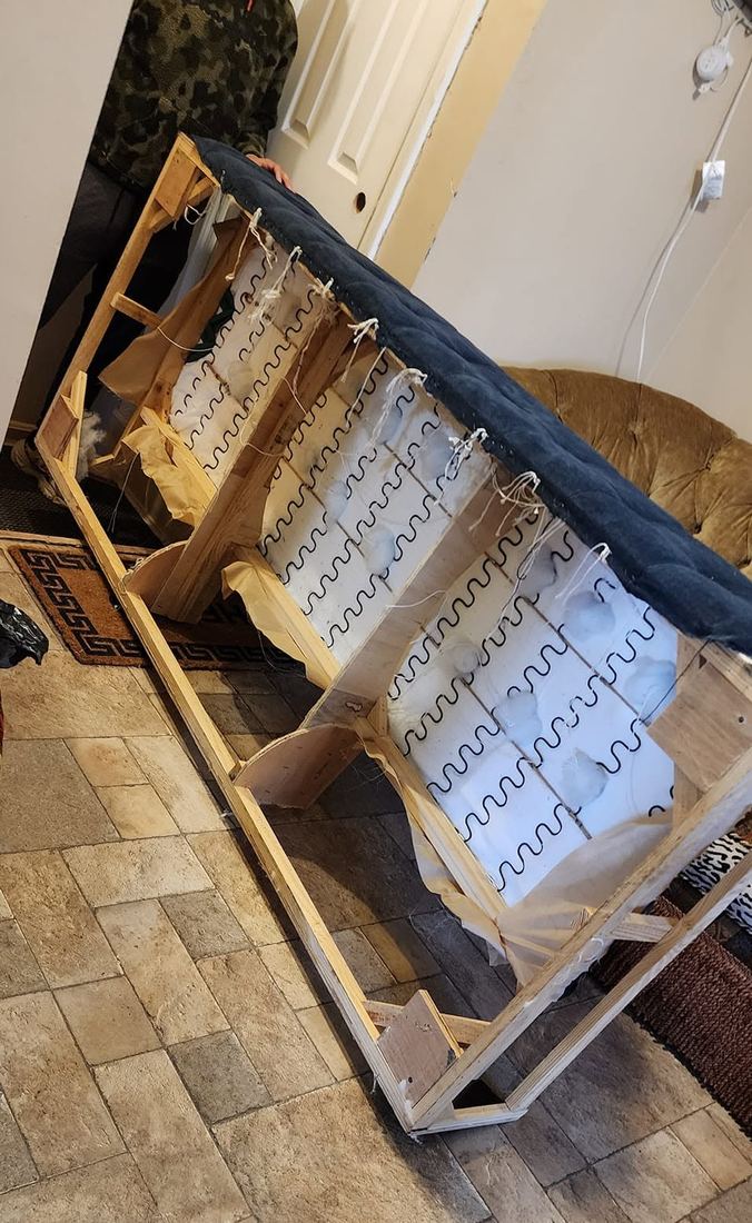 Sofa tipped on its end with the bottom cover open, showing sinuous springs, batting and a wood frame