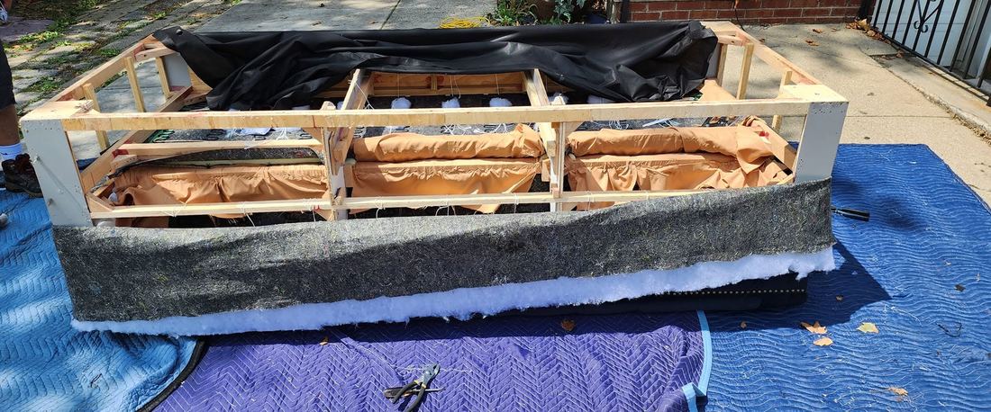 Sofa opened down to its wood frame outdoors on padded blankets, with padding and cover peeled back