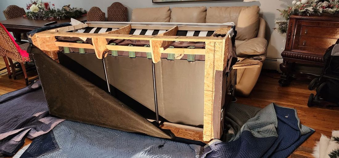 Sofa tipped on padded blankets with the dust cover peeled back, showing the wood frame and webbing